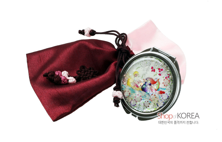 [텍스트: Shop of KOREA 대한민국의 품격까지 전합니다.] 자개 상감 기법의 원앙·꽃문양 금속 손거울과 자주색 비단 복주머니, 배색 매듭 장식 구성