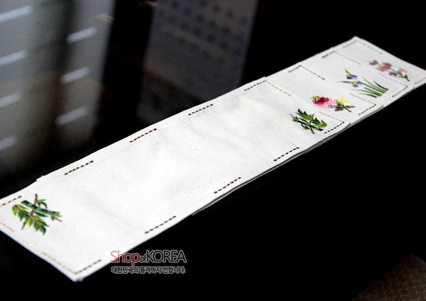 [텍스트: Shop of KOREA 대한민국의 품격까지 전합니다] 광목 재질 화이트 바탕에 매화·대나무 등 꽃과 잎 자수, 컬러 스티치 선이 사각 구획을 이루는 러너형 식탁보 디자인