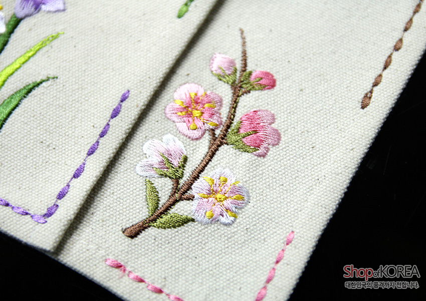 [텍스트: Shop of KOREA 대한민국의 공예작가가 전합니다] 광목 바탕에 갈색 가지와 분홍 매화 자수를 놓고 가장자리를 컬러 스티치 선으로 장식한 전통 자수 식탁보 디테일 모습