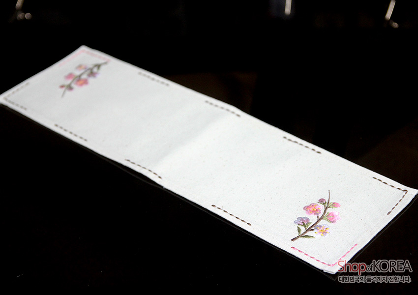 [텍스트: Shop of KOREA 대한민국의 공예가치 전달합니다] 광목 재질 화이트 긴 직사각형 식탁 러너, 양 끝 분홍·연두 매화 자수와 갈색 스티치 테두리 장식 디자인