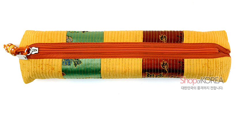 [텍스트: Shop of KOREA, 대한민국의 품격까지 전합니다.] 노란 누비 원단 위 초록·갈색 비단 꽃문양 패치 장식, 주황색 지퍼와 손잡이로 마감한 직사각형 필통 형태 이미지