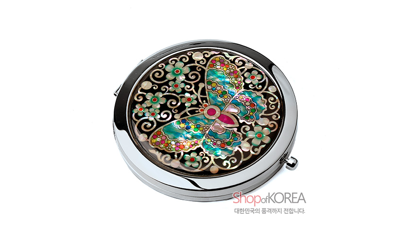 [텍스트: ShopofKOREA, 대한민국의 품격까지 전합니다.] 흑색 바탕 금속 거울 위 다채로운 색감의 자개 상감 채색 나비와 꽃문양 장식 모습
