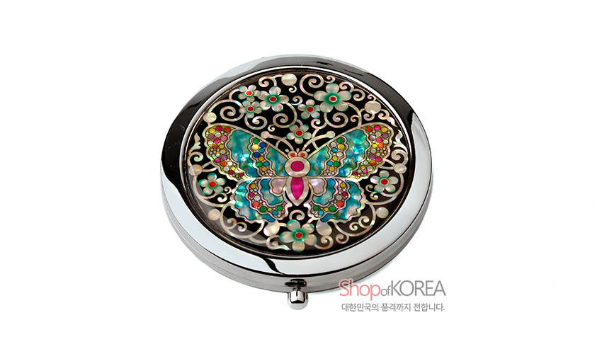 [텍스트: Shop of KOREA 대한민국의 품격까지 전합니다.] 흑색 바탕 위 금속 원형 틀에 자개 상감 기법으로 채색 나비와 꽃문양을 섬세하게 장식한 원터치 손거울 디자인