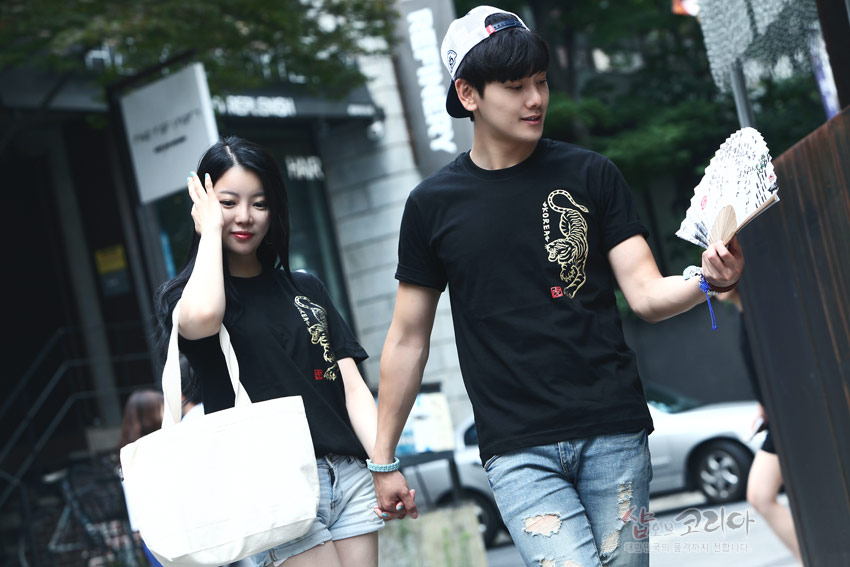 [텍스트: KOREA] 검정 면 티셔츠에 금색 입체발포 호랑이 문양과 붉은 전각 스타일 낙관이 세로 배치된 디자인 연출