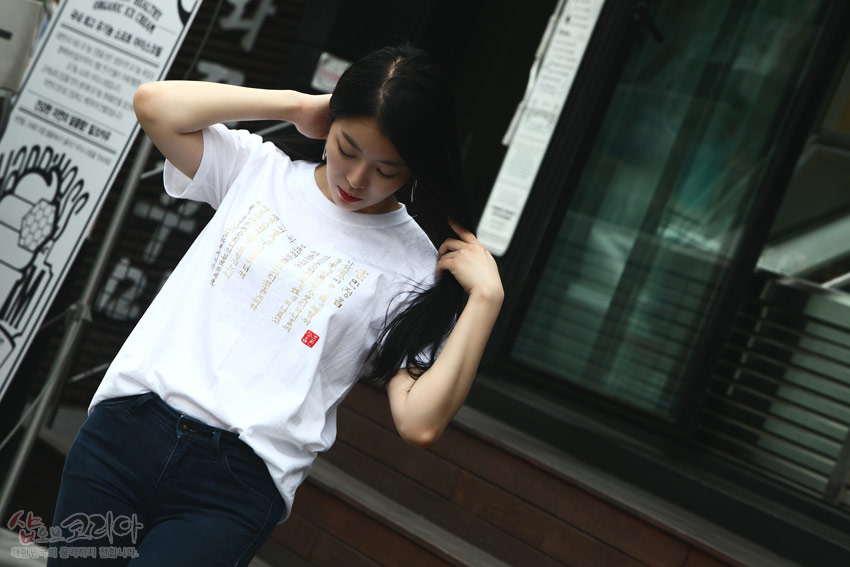 [텍스트: 샵오브코리아 대한민국 전통 문화의 발전을 위해 노력합니다] 흰색 면 티셔츠 위 금빛 입체발포 기법으로 훈민정음 한글·한자 문양과 붉은 낙관 포인트가 조화를 이룬 디자인