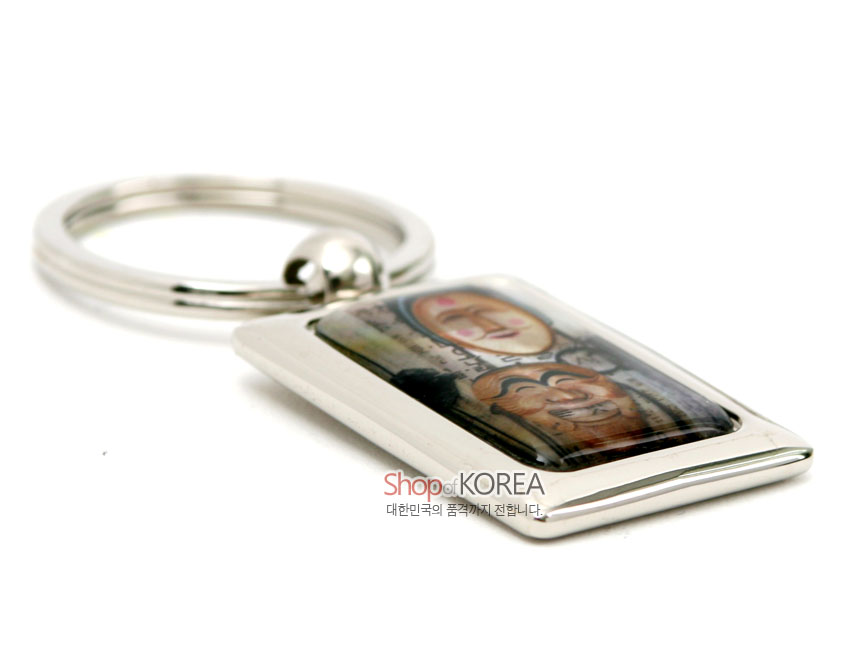 [텍스트: Shop of KOREA 대한민국의 품격까지 전합니다] 은빛 금속 프레임에 자개 상감 기법으로 하회탈 문양을 넣고 유광 코팅으로 마감한 직사각 열쇠고리 디자인