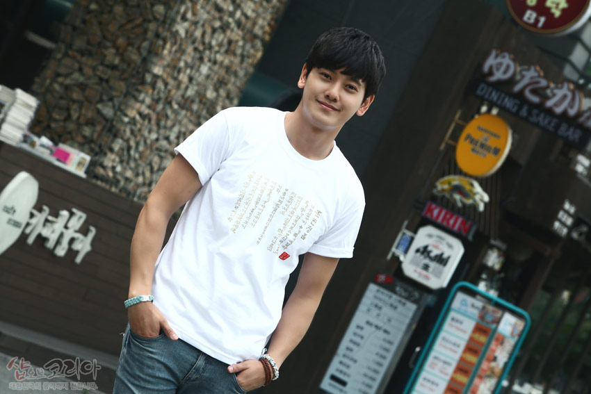 [텍스트: 샵오브코리아 대한민국 전통문화를 전세계에 보냅니다] 흰색 면 티셔츠 중앙에 금빛 입체발포 기법으로 훈민정음 서체 문구가 세로 배열된 디자인