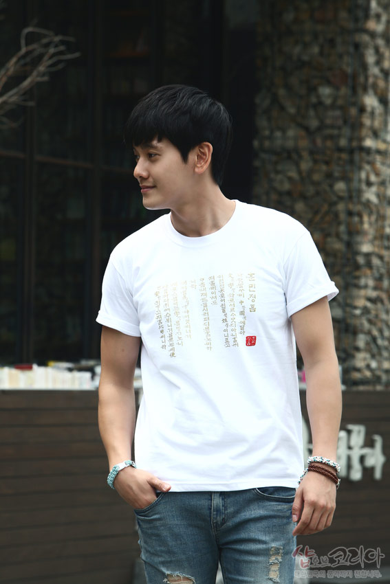 [텍스트: 훈민정음] 흰색 면 티셔츠 위에 금빛 입체발포 기법으로 훈민정음 서문 한글·한자 세로 배열된 전통 서체 문양 디자인