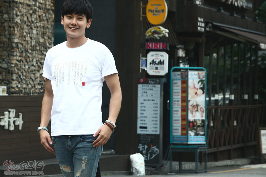 [텍스트: 샵오브코리아 대한민국의 전통지킴이 생각하는] 흰색 면 티셔츠 위 금빛 입체발포 훈민정음 한글·한자 세로 문양과 붉은 낙관 포인트 디자인