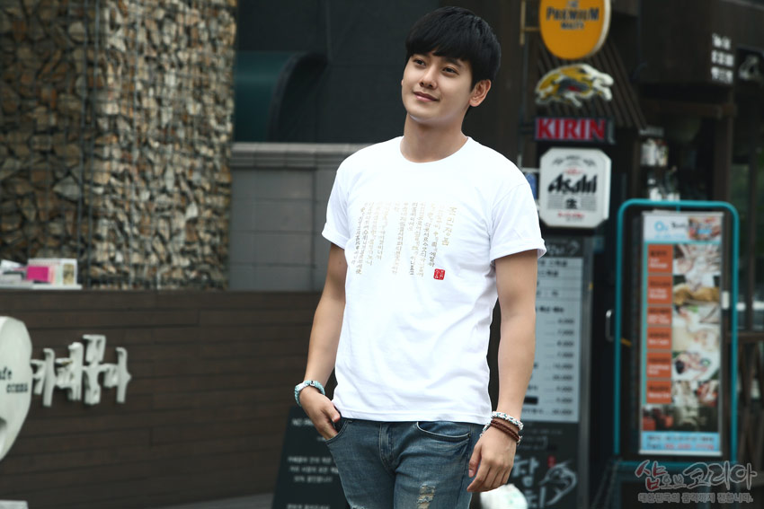 [텍스트: KIRIN] 흰색 면 티셔츠 위 금빛 입체발포 기법으로 표현된 훈민정음 한글·한자 세로 문양과 붉은 색 직사각형 도장 포인트 디자인