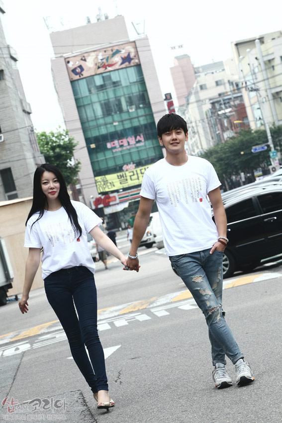 [텍스트: 샵오브코리아] 흰색 면 반소매 티셔츠에 금빛 입체발포 기법으로 훈민정음 한글·한자 서체 문양을 세로 배열로 표현한 디자인