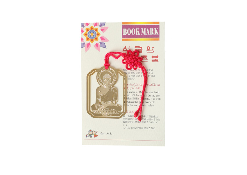 [텍스트: BOOK MARK 석굴암 본존불] 금속 재질에 석굴암 본존불을 정교하게 양각한 금장 책갈피와 붉은 전통 매듭 끈 장식 구성