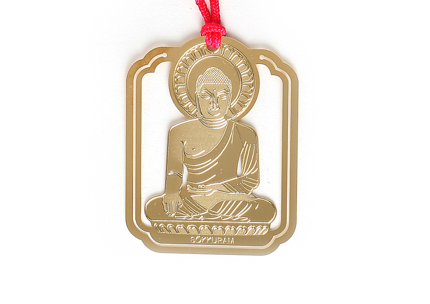 [텍스트: SEOKGURAM] 금속 재질의 금장 프레임에 석굴암 본존불 좌상 문양을 정교한 양각 기법으로 새기고 붉은 전통 매듭 끈을 더한 디자인