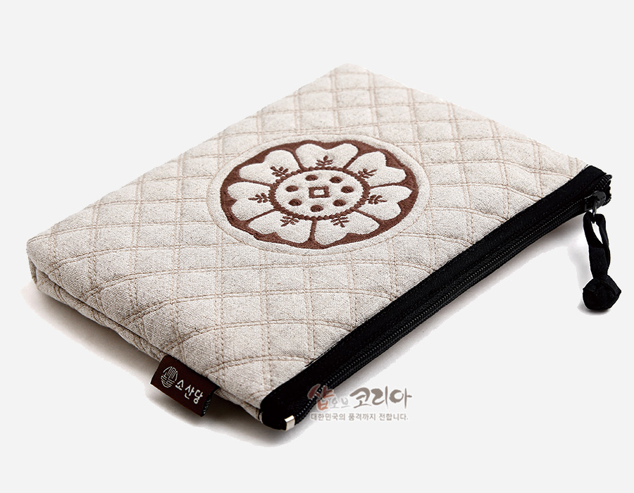 [텍스트: 쇼핑 코리아, 소상당] 베이지색 누빔 원단 위 갈색 백제 수막새 연꽃 문양 자수 장식, 검정 지퍼와 끈 달린 사각 파우치 형태 작품