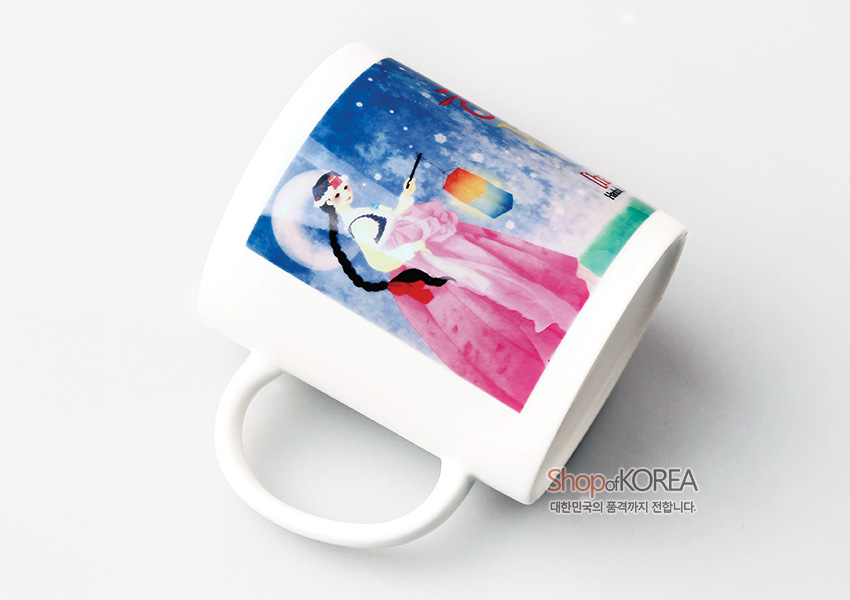 [텍스트: Shop of KOREA 대한민국의 품격까지 전합니다.] 밤하늘 아래 한복 소녀와 청사초롱 일러스트가 인쇄된 도자 머그컵, 파랑과 분홍의 대비가 돋보이는 디자인 묘사