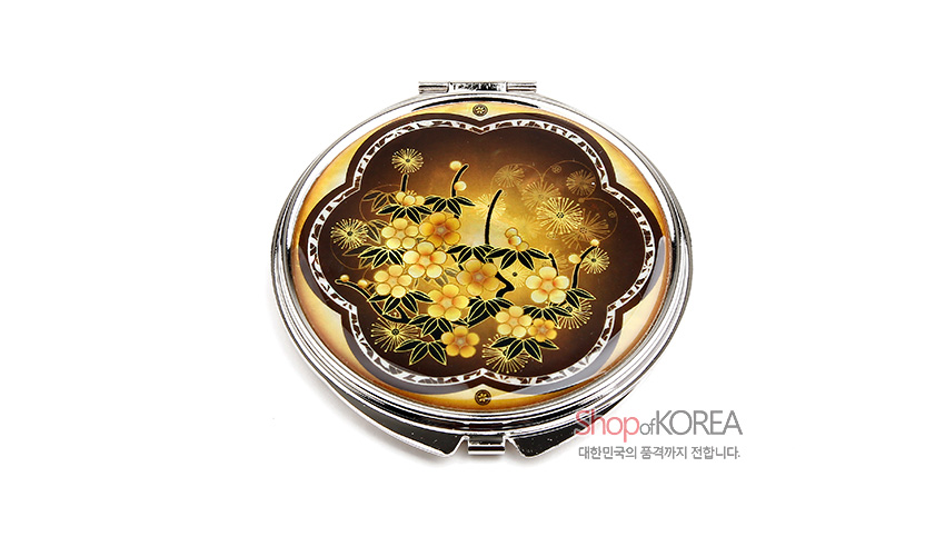 [텍스트: Shop of KOREA 대한민국의 품격까지 전합니다.] 황색과 갈색 그러데이션 바탕 위 자개 상감 기법으로 매화와 잎, 꽃무늬를 정교하게 장식한 금속 테두리 원형 손거울 이미지 설명