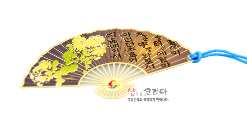 [텍스트: 나랏말ᄊᆞ미 듕귁에 달아 문자와로 서르 사맛디 아니할ᄊᆞ니] 금속 재질 부채형 책갈피에 황금빛 국화 문양과 한글 훈민정음 글귀, 중앙 태극 문양과 하늘색 전통 매듭 장식 구성