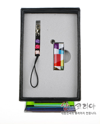 [텍스트: 샵오브코리아 대한민국의 품격까지 전합니다.] 금속 테두리에 다채로운 비단 조각보 패턴을 입힌 직사각형 USB와 오방색 실 매듭 스트랩이 세트로 구성된 포장 상태 이미지 설명
