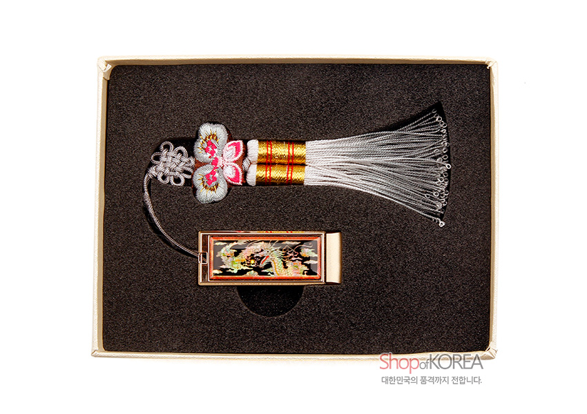 [텍스트: Shop of KOREA 대한민국의 품격까지 전합니다.] 검은 옻칠 바탕 위 자개 상감 황금 용 문양 금속 USB와 분홍·회색 비단 나비매듭, 흰 술 장식이 조화된 전통 매듭 USB 세트 모습