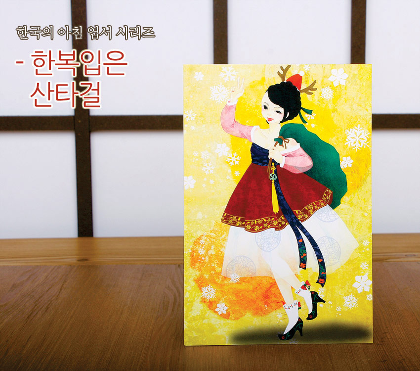 [텍스트: 한국의 아침 엽서 시리즈 - 한복입은 산타걸] 노랑 그라데이션 배경 위에 붉은 한복과 녹색 망토, 사슴뿔 장식 산타 소녀와 흰 눈꽃 문양이 어우러진 일러스트 엽서 이미지 설명