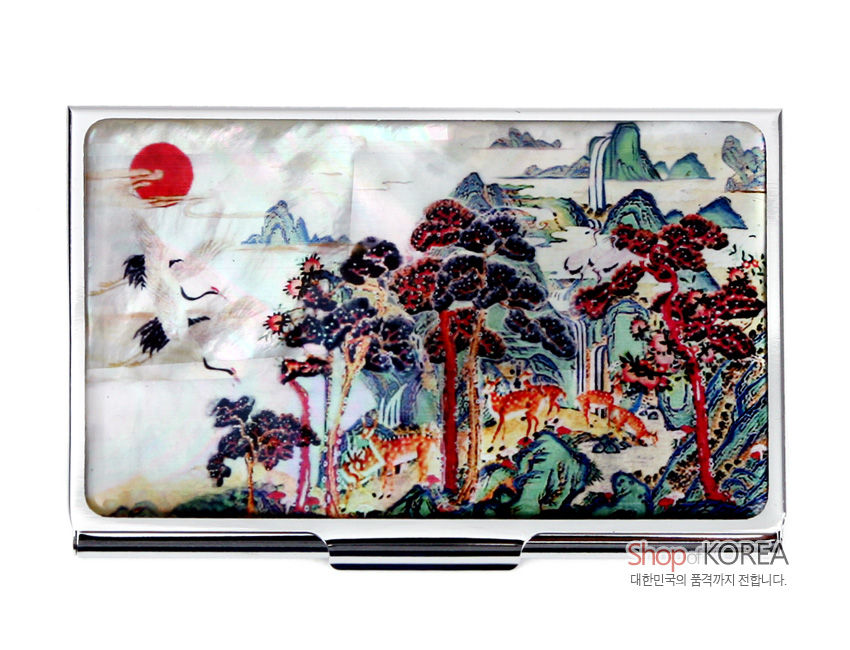 [텍스트: Shop KOREA 대한민국의 품격까지 전합니다.] 자개 바탕 위에 상감 기법으로 표현한 붉은 해, 학, 소나무와 사슴이 어우러진 십장생 민화 산수 문양의 금속 명함집 이미지 설명