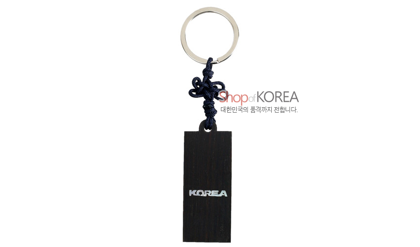 [텍스트: Shop of KOREA, 대한민국의 품격까지 전합니다., KOREA] 흑단 재질 직사각형 열쇠고리에 자개 상감 KOREA 글자와 남색 전통 매듭 장식 구성