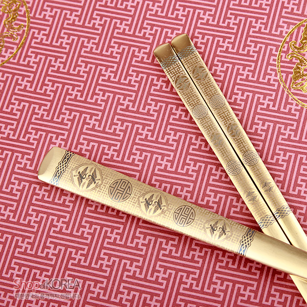 [텍스트: ShopofKOREA] 금빛 티타늄 재질 수저와 젓가락에 십장생과 수복 문자, 기하학 문양을 정교한 음각과 양각으로 장식한 전통 금속 공예 디자인