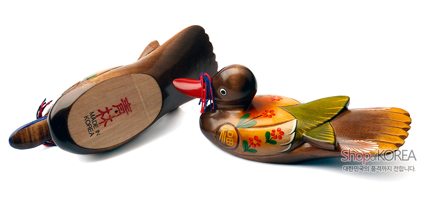 [텍스트: MADE IN KOREA, Shop of KOREA 대한민국의 품격까지 전합니다.] 채색 목재 재질 원앙 한 쌍 장식, 꽃과 복(福)자 문양, 녹색·주황색 날개와 붉은 부리, 청홍 매듭끈 장식 특징의 목각 소품