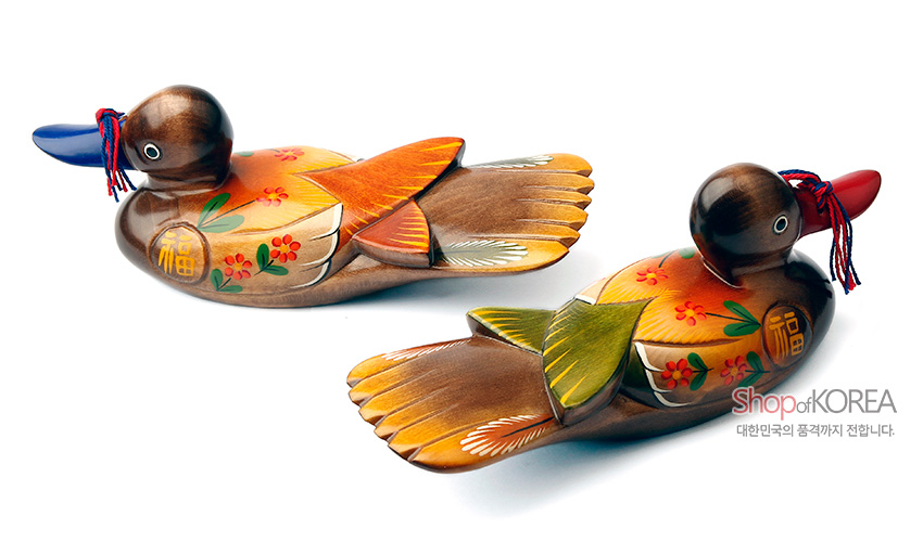 [텍스트: Shop of KOREA, 대한민국의 품격까지 전합니다.] 원목 재질에 채색 기법으로 표현된 꽃무늬와 복(福)자 문양, 붉은 술 장식이 더해진 원앙 한 쌍 목각 장식품