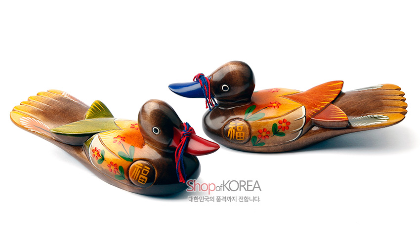 [텍스트: ShopofKOREA 대한민국의 품격까지 전합니다.] 원목 재질에 채색 기법을 더한 원앙 한 쌍 목각 장식, 붉은 끈과 꽃·복(福)자 문양, 노랑·초록·주황 대비 색감이 돋보이는 전통 장식품