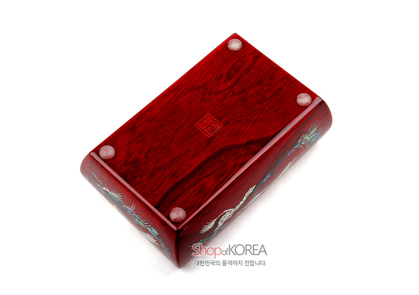 [텍스트: Shop of KOREA 대한민국의 품격까지 전합니다.] 붉은 옻칠 나무 바탕에 자개 상감으로 학과 소나무 문양을 둘레에 장식한 직사각 반지함 바닥면 디자인