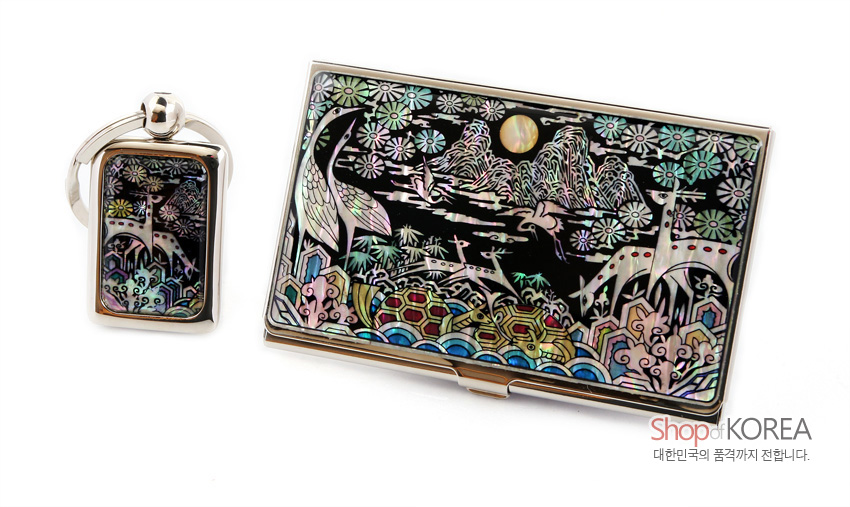 [텍스트: Shop of KOREA 대한민국의 품격까지 전합니다.] 흑색 옻칠 바탕 위 자개 상감으로 학·사슴·거북과 산수, 십장생꽃무늬를 표현한 금속 명함집과 열쇠고리 세트 이미지