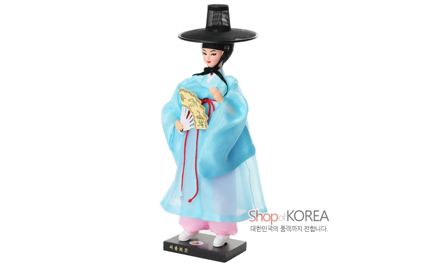 [텍스트: Shop of KOREA / 대한민국의 품격까지 전합니다.] 하늘색 비단 도포와 분홍 바지, 붉은 매듭끈 장식, 검은 갓과 전통 문양 부채를 든 조선 선비 한복인형 모습