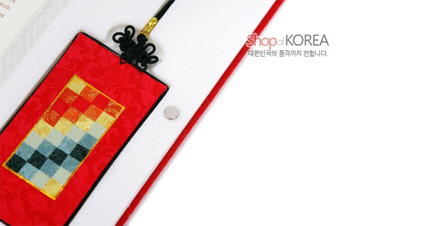 [텍스트: Shop of KOREA 대한민국의 품격까지 전합니다.] 붉은 비단 바탕 위 다채로운 격자무늬 조각보 패턴과 흑색 전통 매듭 장식의 직사각 책갈피 이미지 설명