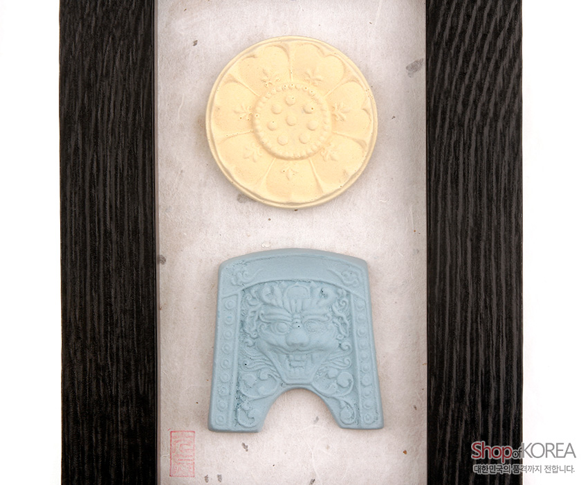 [텍스트: Shop of KOREA 대한민국의 품격까지 전합니다.] 검은 나무 액자에 흰 한지 바탕, 황색 연꽃무늬 원형 향 장식과 청색 귀면문 양각 장식 배치된 구성