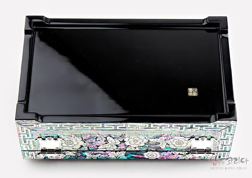[텍스트: 샵오브코리아 대한민국의 품격까지 전합니다] 흑색 옻칠 상판과 측면 전면에 자개 상감으로 표현된 꽃과 나비, 연속 기하학 문양이 어우러진 직사각 보석함 디자인