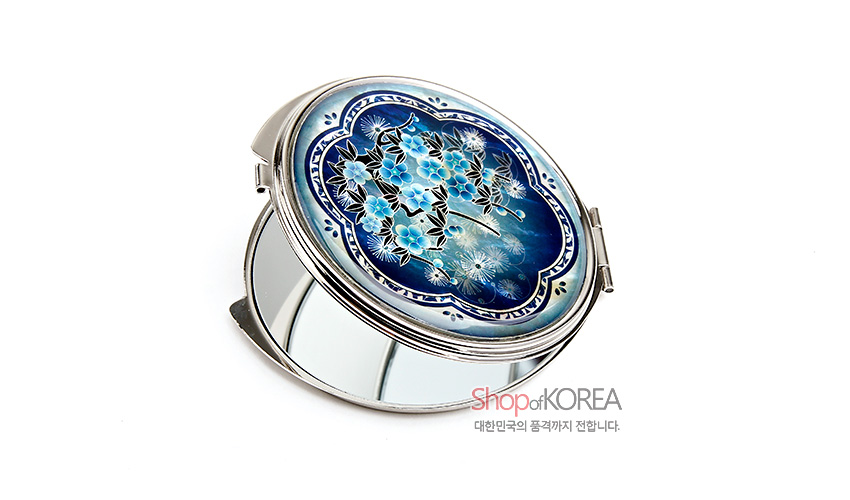 [텍스트: Shop of KOREA, 대한민국의 품격까지 전합니다.] 청색 그라데이션 바탕 위 자개 상감 기법으로 매화와 민들레 문양을 섬세하게 표현한 금속 테두리 원형 손거울 디자인