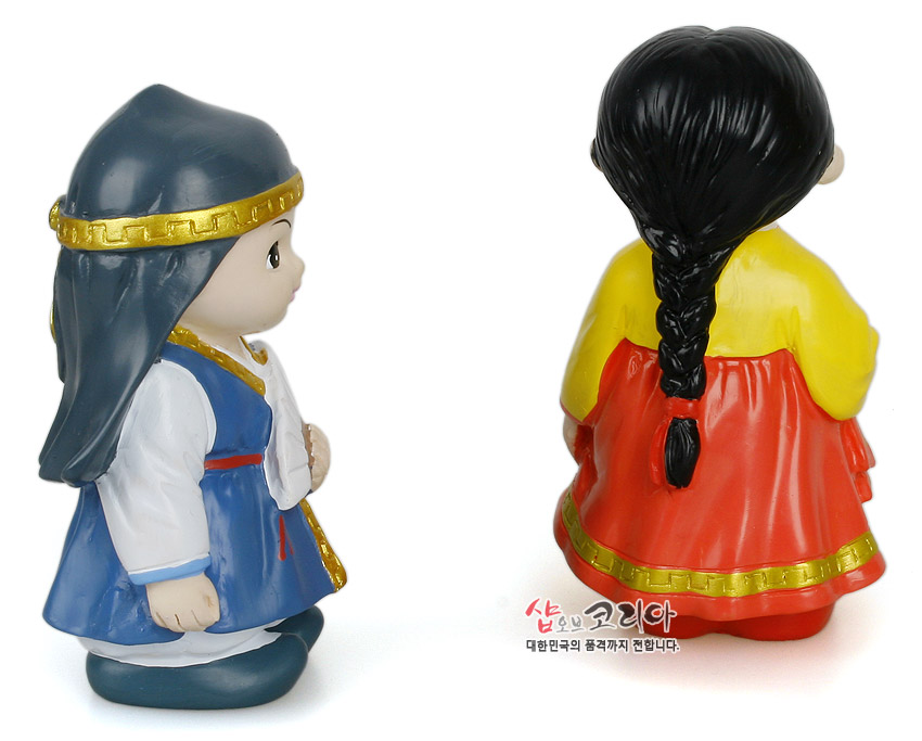 [텍스트: 샵오브코리아 대한민국의 품격까지 전합니다.] 채색 플라스틱 재질 춘향·몽룡 한복 인형, 금색 띠 장식과 대비되는 청색·홍색·노랑 색채, 땋은 머리 표현이 특징인 민속 인형 연출