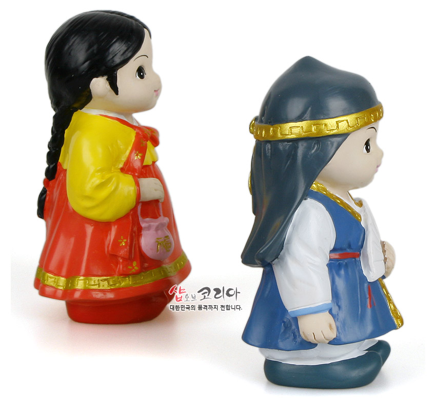 [텍스트: 샵오브코리아 대한민국의 품격까지 전합니다.] 채색 플라스틱 재질의 춘향·몽룡 인형, 노란 저고리와 붉은 치마, 파란 도포와 금색 테두리 장식이 대비를 이루는 민속풍 한복 인형 모습