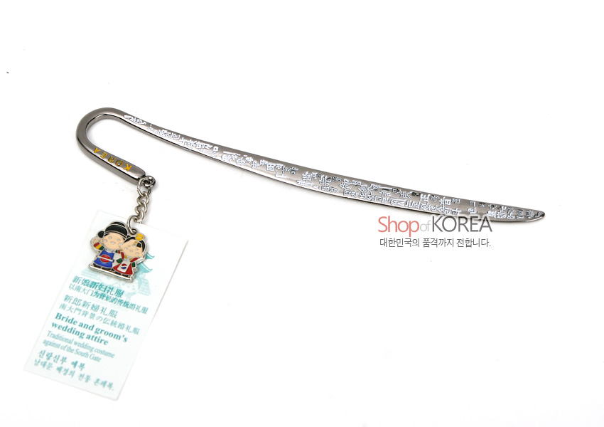 [텍스트: Shop of KOREA 대한민국의 품격까지 전합니다. Bride and groom’s wedding attire Traditional wedding couple] 은빛 금속 재질의 길게 휘어진 책갈피에 한글 문양 양각 장식과 한복 예복 신랑신부 캐릭터 에나멜 장식 매달린 디자인