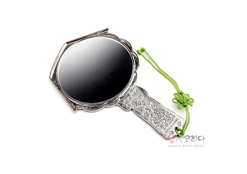 [텍스트: 샵오브코리아 대한민국의 품격까지 전합니다.] 금속 재질 손잡이에 섬세한 꽃문양이 양각된 원형 손거울, 연두색 전통 매듭끈 장식 구성