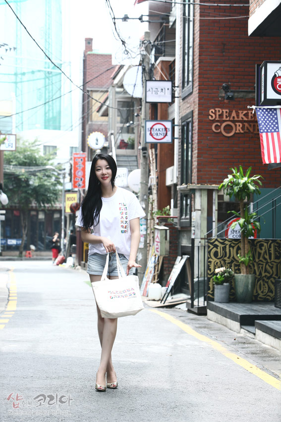 [텍스트: SPEAKER’S CORNER, 서궁치] 흰색 면 티셔츠 위 다채로운 색상의 한글 자음 세로 배치와 입체 발포 프린트가 돋보이는 캐주얼 거리 패션 연출 모습