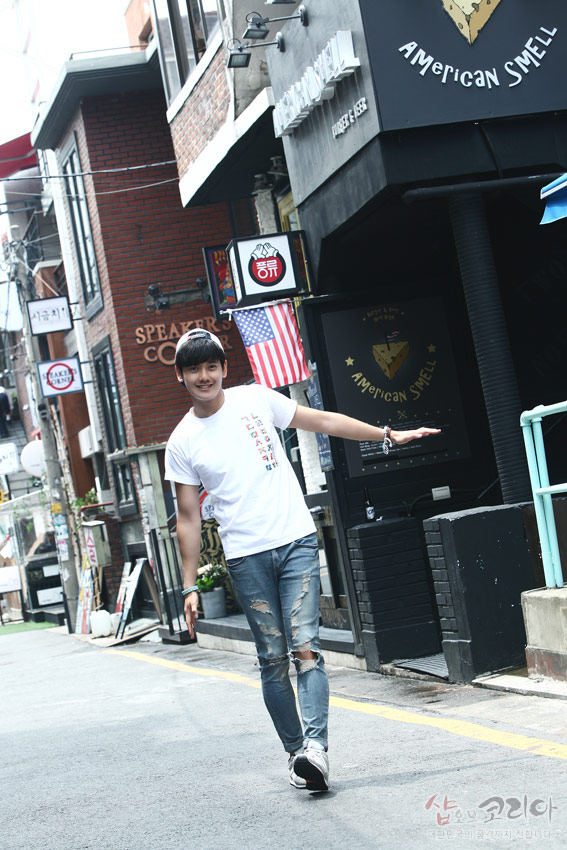 [텍스트: American SMELL / 샵오브코리아] 흰색 면 티셔츠 위 세로 배열 다채로운 한글 자음 입체발포 프린트와 캐주얼한 거리 풍경 대비 모습