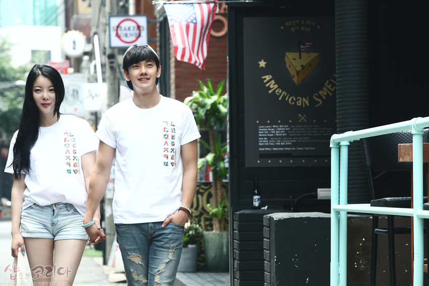 [텍스트: AMERICAN SMEL] 흰색 면 티셔츠 중앙에 다채로운 색감의 한글 자음을 세로 배열로 입체 발포 인쇄한 캐주얼 반팔 티셔츠 연출