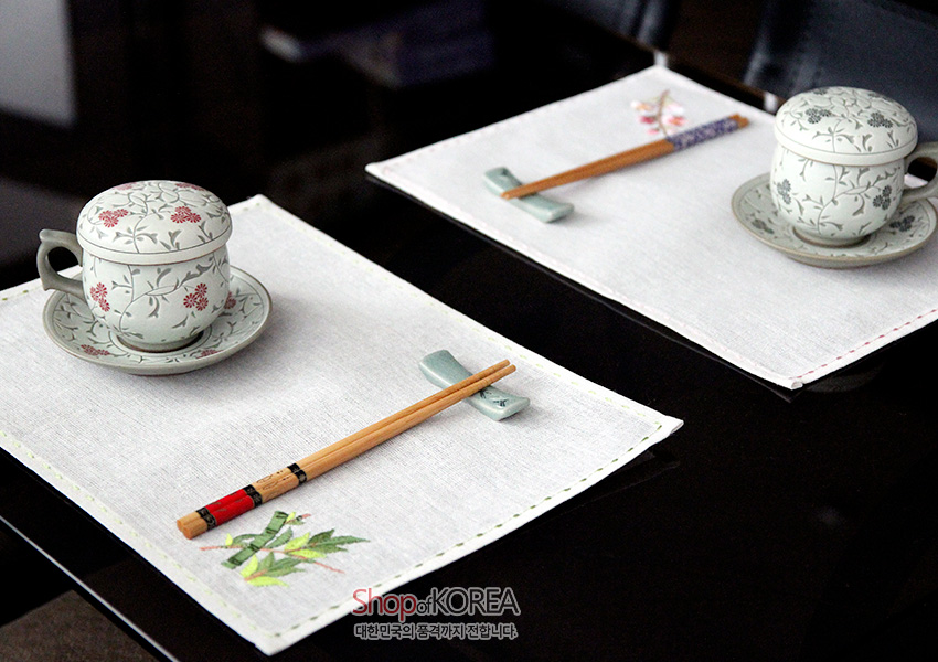 [텍스트: Shop of KOREA 대한민국의 품격까지 전합니다] 옅은 회색 모시 재질 위 가장자리 컬러 스티치와 대나무·매화 자수 문양이 놓인 사군자 식탁 매트 구성
