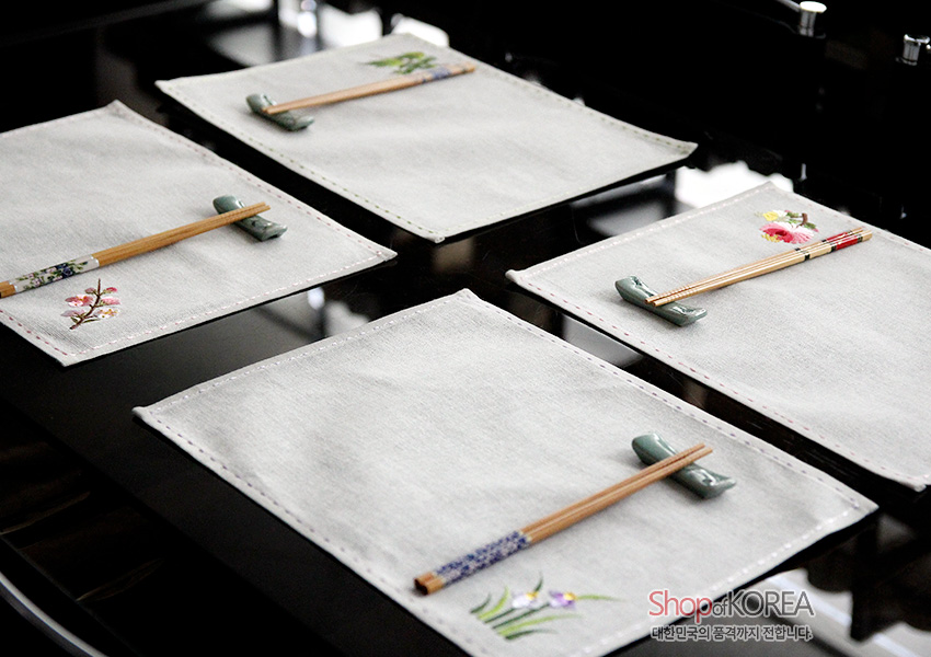 [텍스트: ShopofKOREA 대한민국의 품격까지 전달합니다] 옅은 회색 모시 식탁매트에 사군자 자수 문양과 색실 스티치, 대나무 젓가락과 도자기 수저받침 구성 연출 이미지