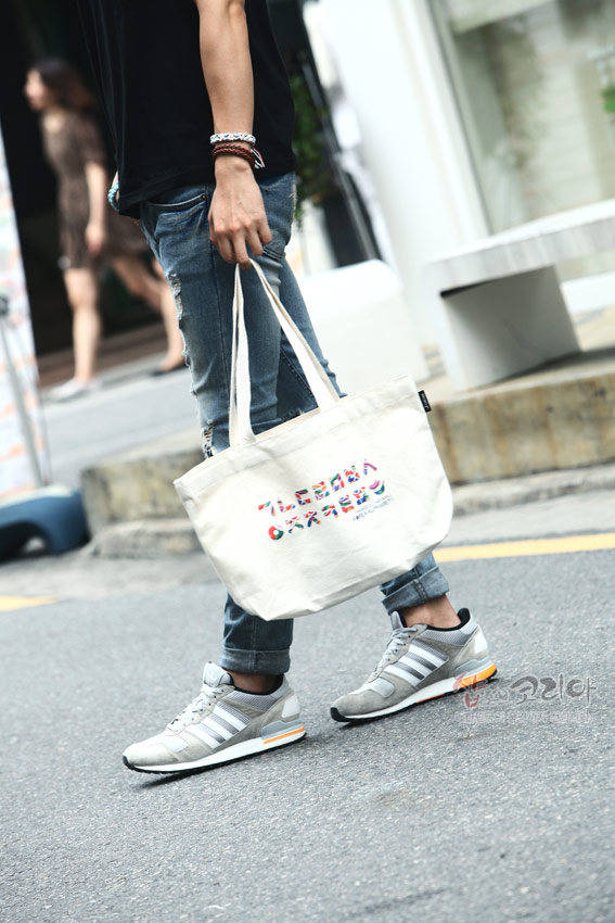 [텍스트: 가 나 다 라 마 바 사] 거리에서 연청 데님과 흑색 상의를 착용한 인물이 한글 자음 컬러 프린트 캔버스 에코백을 들고 있는 모습의 연출 컷