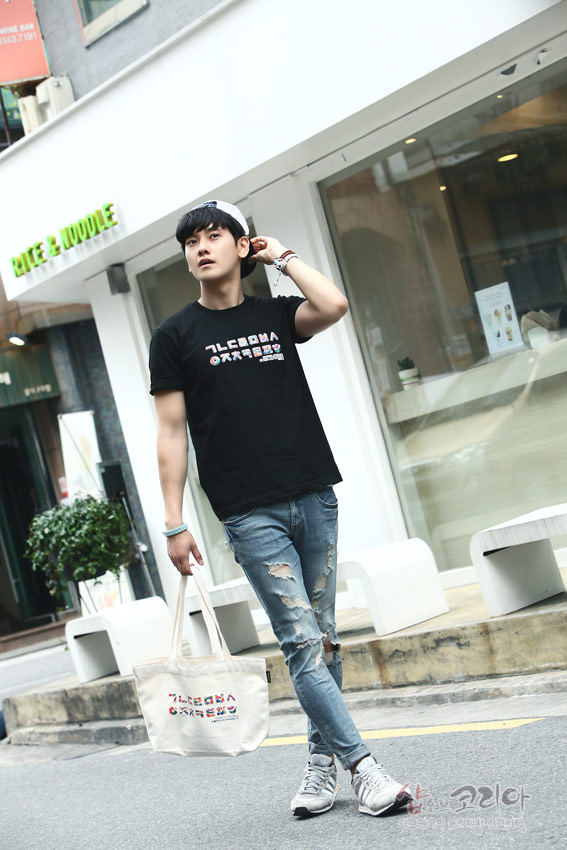 [텍스트: 가나다라마바사 아자차카타파하] 검정색 면 티셔츠에 한글 자음 가로 배열 3D 입체발포 프린트가 들어간 캐주얼 스타일 연출 모습