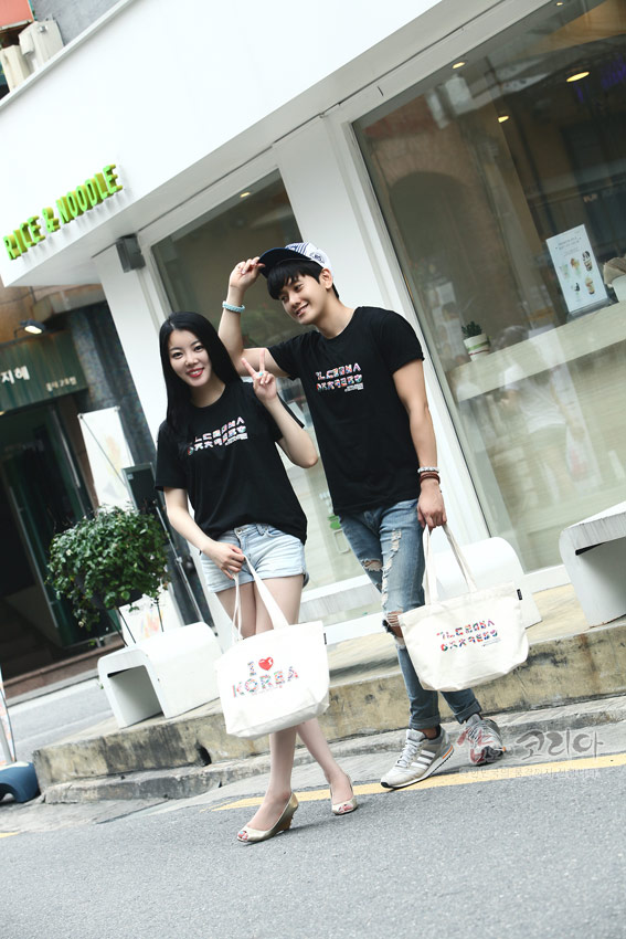 [텍스트: KOREA] 흑색 면 소재 위 한글 자음 가로 배열 3D 입체발포 프린트가 들어간 반소매 티셔츠와 아이보리색 코튼 가방 연출 이미지