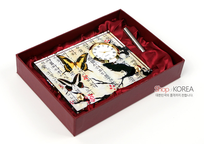 [텍스트: Shop of KOREA 대한민국의 품격까지 전합니다.] 자개 느낌 바탕 위 매화 가지와 나비 문양, 한글 서체가 어우러진 탁상용 금속 테두리 시계와 펜 세트 구성